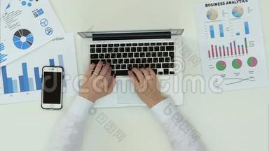 女人`在办公室桌上的笔记本电脑上打字，上面有统计表
